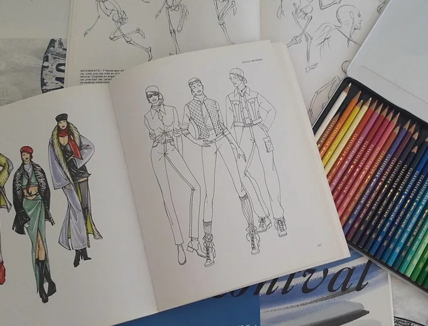Open sketchbook with figure drawings next to a tin of coloured pencils