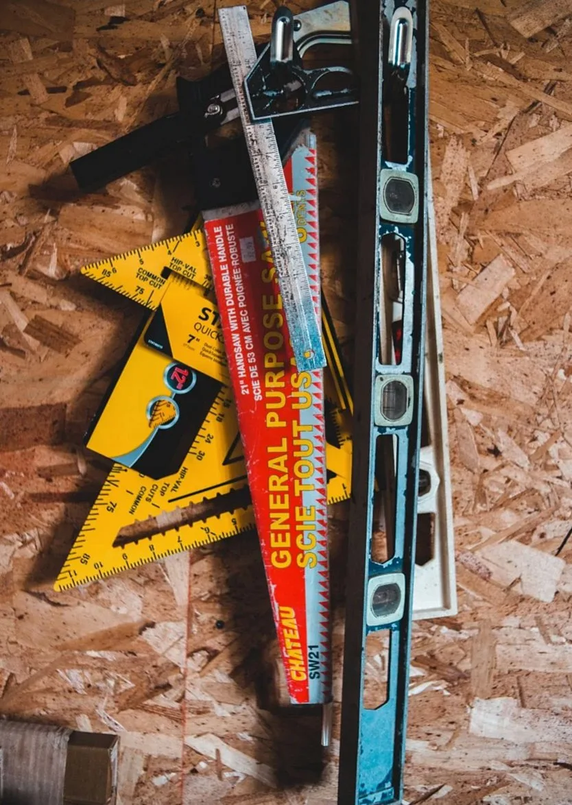 Measuring tools and a hand saw lying on a plywood panel